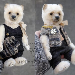 May include: A cream-colored plush bear with dark eyes and a stitched nose, wearing black pinstriped overalls and a beige ribbon. The bear is shown with a gray and brown knit vest featuring a white snowflake button. Text reads BEARS HAPPY HEART.