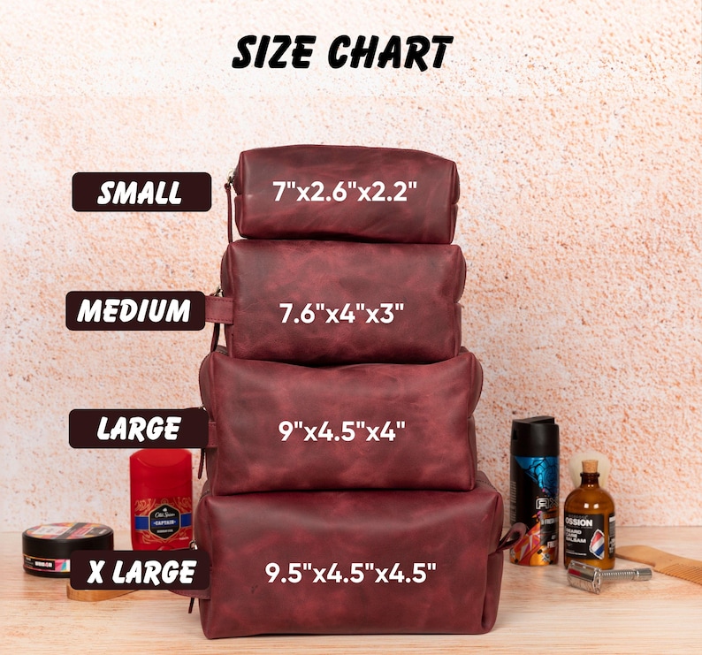 Op de afbeelding: Een maattabel toont vier bordeauxrode leren toilettassen in verschillende maten: klein (17.8cm x 6.6cm x 5.6cm), medium (19.3cm x 10.2cm x 7.6cm), groot (22.9cm x 11.4cm x 10.2cm) en extra groot (24.1cm x 11.4cm x 11.4cm). De tekst "SIZE CHART" staat bovenaan.