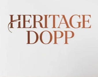May include: The words "HERITAGE DOPP" are displayed in a copper-colored font against a white background. The text is centered and the font is a serif style. The overall design is simple and elegant.