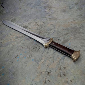 May include: A handcrafted dagger featuring a polished steel blade and a dark wood handle. The handle has brass fittings. The blade is about 30 cm long, and the design suggests a historical or fantasy theme.