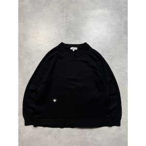 Può includere: Maglione nero a maniche lunghe con girocollo. Un piccolo emblema bianco è sul petto. Il maglione è realizzato in un tessuto morbido e strutturato. Lo sfondo è grigio neutro.