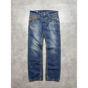May include: Blue denim jeans featuring a faded wash, a button fly closure, and prominent gold-tone contrast stitching along the seams and pockets. The jeans include five pockets, belt loops, and a metal button at the waist with a classic straight leg cut.