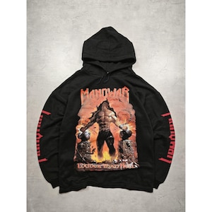 Könnte beinhalten: Schwarzer Kapuzenpullover mit einer Grafik einer muskulösen Figur, dem Wort "MANOWAR" darüber und "LOUDER THAN HELL" darunter. Roter Text ist auf den Ärmeln aufgedruckt. Der Pullover ist aus weichem Material.