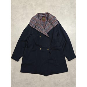 Puede incluir: Un abrigo azul marino de doble botonadura con cuello estampado. El abrigo presenta dos filas de botones dorados, dos bolsillos delanteros y un cuello con un estampado geométrico en tonos morado, marrón y azul.