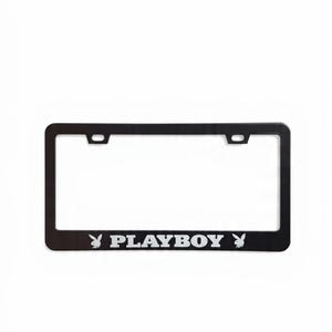Puede incluir: Marco negro para matrícula con la palabra "PLAYBOY" en letras plateadas y el logotipo del conejo. El marco es rectangular con un borde sólido y orificios de montaje.