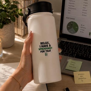 Pode incluir: Uma garrafa de água térmica branca com tampa preta e um adesivo que diz "RELAX, I HAVE A SPREADSHEET FOR THAT" em texto preto e verde, acompanhado por um pequeno ícone verde de planilha. A garrafa possui um acabamento fosco e suave.