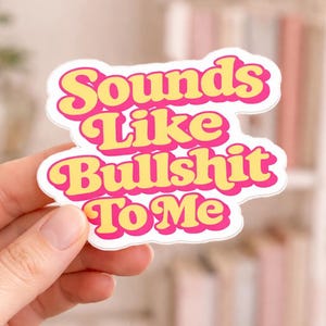 May include: A die-cut sticker featuring the text Sounds Like Bullshit To Me in a bold, retro-inspired font. The lettering is yellow with a thick, vibrant pink outline, set against a clean white background with a wavy, organic border shape.