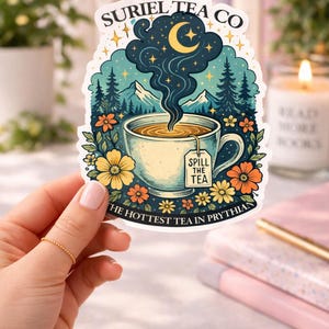 May include: A die-cut sticker featuring a teacup with steam rising into a night sky with a crescent moon and stars. The text reads SURIEL TEA CO at the top, SPILL THE TEA on the tea bag tag, and THE HOTTEST TEA IN PRYTHIAN at the bottom.