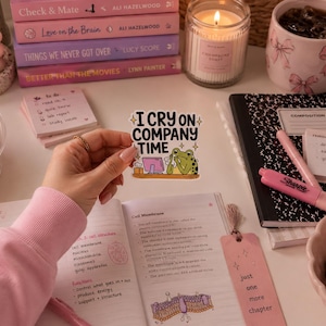 May include: A die-cut vinyl sticker featuring a green frog sitting at a computer desk, holding a tissue to its face, with the text "I CRY ON COMPANY TIME" in bold black letters, accented by small yellow stars on a white background.