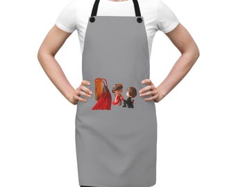 May include: A gray apron with black straps featuring a decorative design. The design includes a red tassel, a bride in a red dress, and a groom in a black suit. The apron is worn by a person.