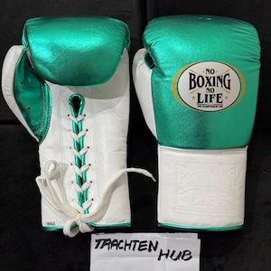May include: Pair of boxing gloves with white and green metallic accents. The gloves feature white laces and cuffs, with the text "NO BOXING NO LIFE" on one glove. The gloves are on a dark surface.
