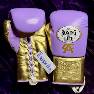 May include: A pair of purple and gold boxing gloves with white laces. The gloves have the text "No Boxing No Life" on them.