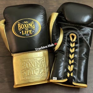 May include: Pair of black and gold boxing gloves. The gloves have gold accents and the text "NO BOXING NO LIFE TEAM" is printed on the front. The gloves are 14 oz.