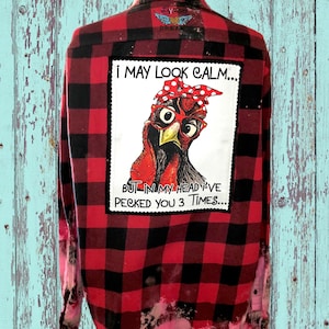 May include: Red and black plaid flannel shirt with a patch on the back that says "I may look calm... but in my head I've pecked you 3 times..." and features a cartoon chicken wearing glasses and a red and white polka dot bandana.