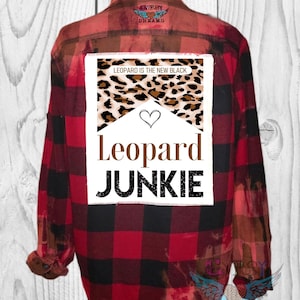 May include: Red and black plaid flannel shirt with a white patch on the back that says "Leopard is the new black" with a leopard print design and a heart. The patch also says "Leopard Junkie" in brown letters.