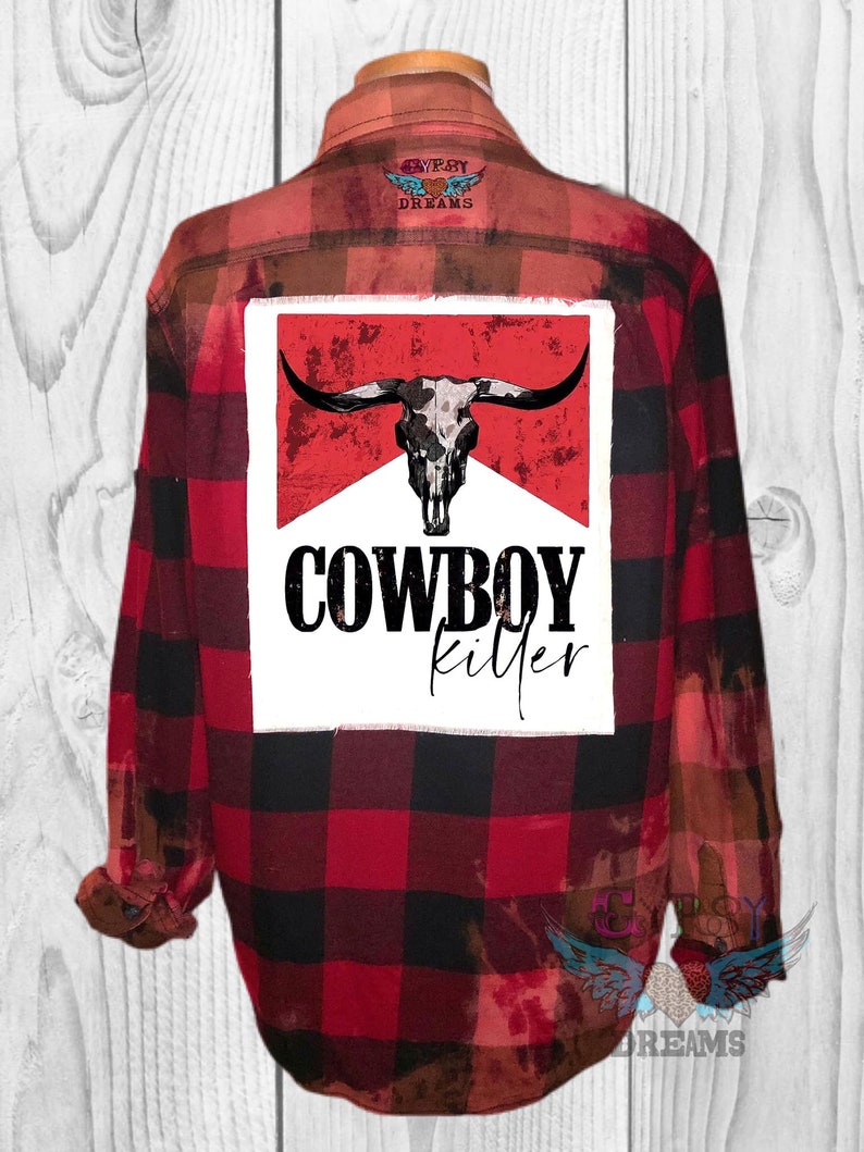 May include: Red and black plaid flannel shirt with a white patch on the back that says "COWBOY killer" with a skull and horns graphic.