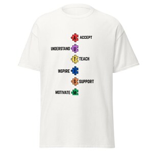 May include: White t-shirt with a graphic of colorful puzzle pieces spelling out "ACCEPT, UNDERSTAND, TEACH, INSPIRE, SUPPORT, MOTIVATE"