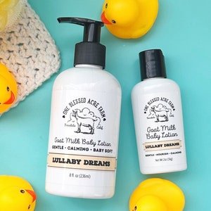 May include: Two bottles of goat milk baby lotion from One Blessed Acre Farm. The larger bottle is 8 fluid ounces and the smaller bottle is 2 ounces. Both bottles have a white label with black text and a drawing of a goat. The text on the label says "Goat Milk Baby Lotion" and "Lullaby Dreams".