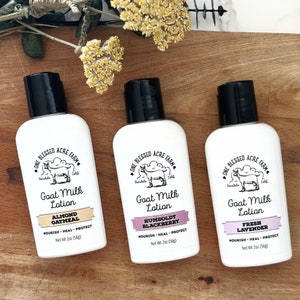 May include: Three white bottles of goat milk lotion with black lids and labels. The labels feature a goat illustration and the text "One Blessed Acre Farm". The lotion flavors are Almond Oatmeal, Humboldt Blackberry, and Fresh Lavender.