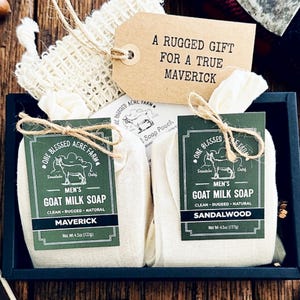 Puede incluir: Un juego de regalo con dos jabones de leche de cabra en bolsas de muselina, etiquetados como "Maverick" y "Sandalwood". El juego incluye un paño de lavado de fibra natural y una etiqueta que dice "Un regalo rudo para un verdadero Maverick".