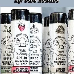 May include: A close-up of six lip balm tubes with different flavors. The tubes are black with white labels. The labels feature a goat, a strawberry, and a whipped cream design. The text on the labels reads "One Blessed Acre Farm", "Milk 'n Honey SPF 30 Sunscreen Lip Balm", "Summer Strawberry", "Fresh Cream", "Farmhouse Mint", and "Milk 'n Honey SPF 30 Sunscreen Lip Balm".