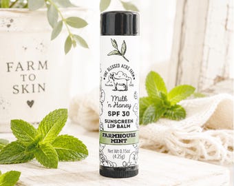 May include: A cylindrical lip balm tube with a black cap and base. The white label features a goat illustration, the text One Blessed Acre Farm, Milk 'n Honey, SPF 30, Sunscreen Lip Balm, and Farmhouse Mint. The net weight is 4.25g (0.15oz).