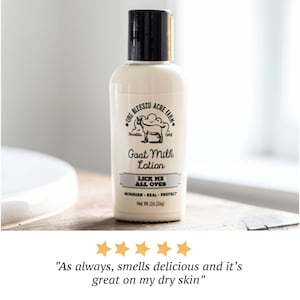 K&ouml;nnte beinhalten: Eine wei&szlig;e Flasche Ziegenmilch-Lotion mit schwarzem Deckel. Das Etikett zeigt eine Ziegenillustration und den Text "LICK ME ALL OVES". Die Flasche steht auf einer Holzoberfl&auml;che. Nettogewicht 59g.