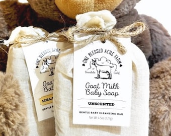Puede incluir: Dos bolsas de muselina de jabón para bebés con leche de cabra sin perfume, cada una con una etiqueta con una ilustración de cabra y el texto "One Blessed Acre Farm". Las bolsas están atadas con hilo.