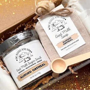 Könnte beinhalten: Eine Geschenkbox gefüllt mit einer braunen Papiertüte, die eine Seife aus Ziegenmilch mit dem Text "One Blessed Acre Farm Goat Milk Soap Almond Oatmeal Natural Exfoliating Bar Net Wt 4 oz (117g)" enthält. Die Box enthält auch ein Glas Ziegenmilch-Zuckerschrub mit dem Text "One Blessed Acre Farm Ferndale Calif Goat Milk Sugar Scrub Refresh Rejuvenate Renew Almond Oatmeal Net Wt 6oz (170g)" und einen Holzlöffel.