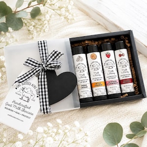 May include: A gift box containing four lip balm tubes labelled Milk 'n Honey Sun Protection Lip Balm in Fresh Cream, Wild Orange, Summer Strawberry, and Black Cherry, each 4.25g. A black heart tag and black and white gingham ribbon are attached.