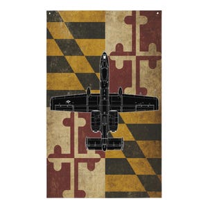 May include: A vertical flag featuring the Maryland state flag design with a black outline of an A-10 Thunderbolt II aircraft. The flag has a distressed, vintage appearance with the Maryland flag's black, gold, red, and white color scheme.