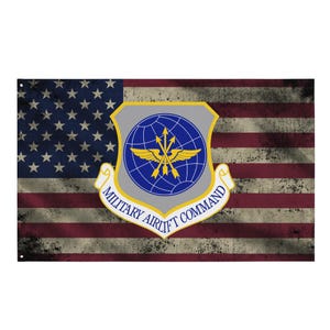 Może przedstawiać: Zniszczona flaga amerykańska z emblematem Military Airlift Command. Flaga ma wzór gwiazd i pasków z wyblakłym, vintage'owym wyglądem. Emblemat to tarcza z globusem i skrzydłami.