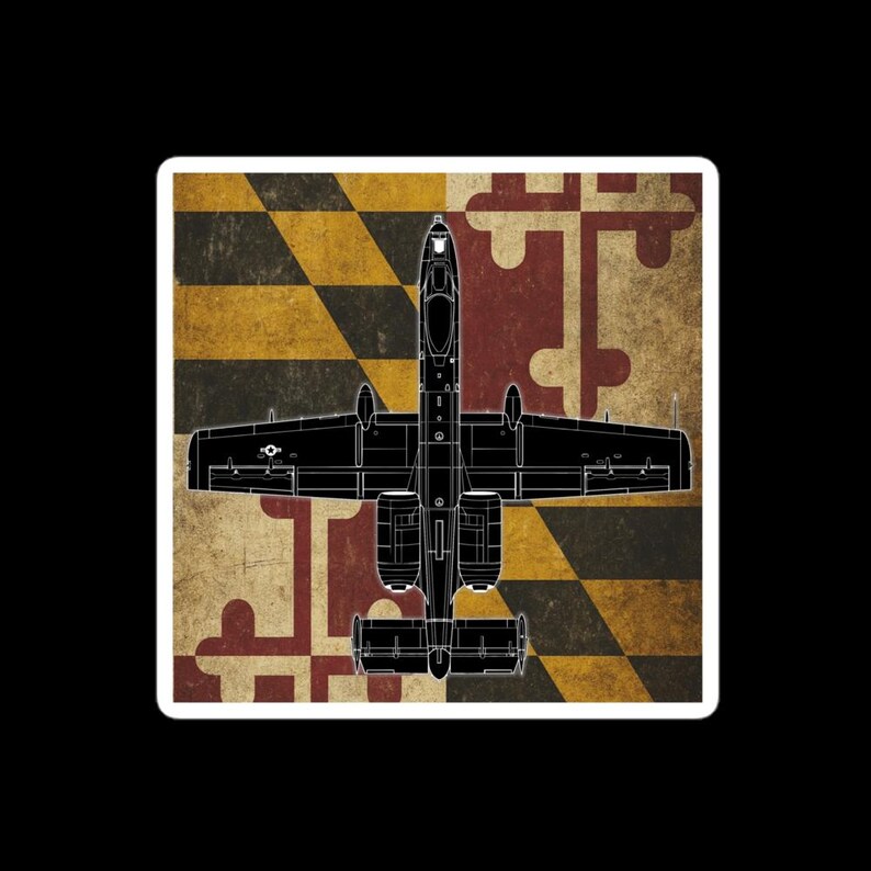 May include: A black outline of an A-10 Thunderbolt II aircraft is centered on a sticker. The background features the Maryland state flag design in red, yellow, black, and white. The sticker has a white border and a black background.