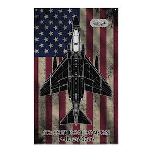 May include: A distressed American flag with a black silhouette of an F-4D Phantom jet aircraft. The text "CC: SSGT DON DONSON F-4D 66-0266" is printed below the aircraft.