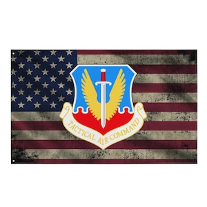 Może przedstawiać: Zniszczona flaga amerykańska z emblematem Tactical Air Command. Emblemat przedstawia miecz, skrzydła i napis "Tactical Air Command". Flaga ma wygląd vintage, znoszony i wyblakłymi kolorami.