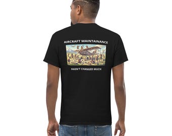 May include: A black t-shirt featuring a white graphic of a vintage aeroplane being worked on by people in period clothing. The text "Aircraft Maintainance Hasn't Changed Much" is printed below the image.