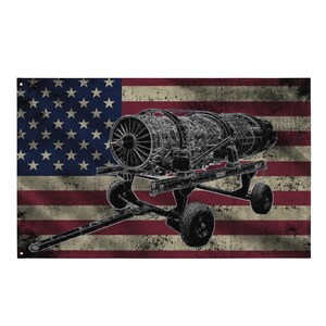 Könnte beinhalten: Schwarz-weiße Illustration eines Strahltriebwerks auf einem rollbaren Wagen, vor einem verwitterten Hintergrund der amerikanischen Flagge. Die Flagge zeigt rote und weiße Streifen und ein blaues Feld mit weißen Sternen. Das Bild hat eine Vintage-Ästhetik.