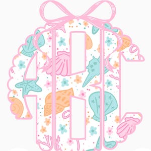 May include: A pink and white beach-themed monogram design with the text "Beach Monogram". The monogram is filled with seashells, starfish, and floral patterns in pastel colors. A pink bow tops the design.