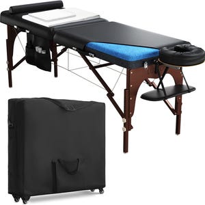May include: A black and brown massage table with a headrest, armrests, and a carrying case. The table has a black padded surface with a blue foam layer visible. The wooden frame is dark brown.