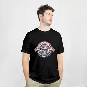 Puede incluir: Camiseta negra con un dise&ntilde;o circular que presenta una calavera, elementos de la bandera estadounidense y el texto "UNITED WE STAND, BOLD, BRAVE, FREE". El dise&ntilde;o utiliza los colores rojo, blanco y azul.