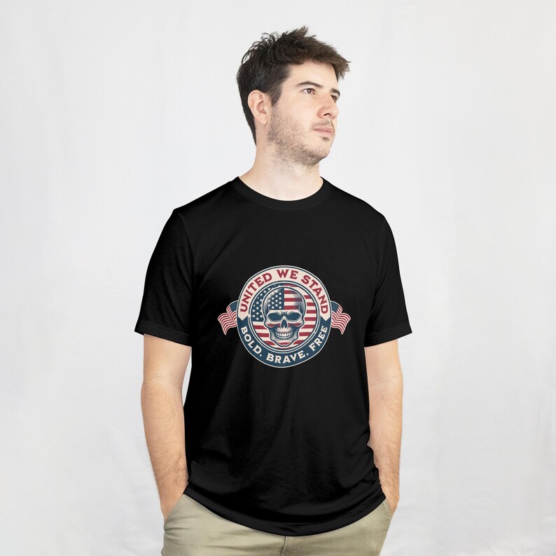 Puede incluir: Camiseta negra con un dise&ntilde;o circular que presenta una calavera, elementos de la bandera estadounidense y el texto "UNITED WE STAND, BOLD, BRAVE, FREE". El dise&ntilde;o utiliza los colores rojo, blanco y azul.