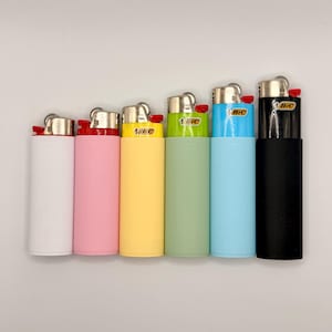 May include: A set of six Bic lighters arranged in a row, featuring matte-finish sleeves in white, pink, yellow, light green, light blue, and black. Each lighter has a metallic top, a red ignition button, and the Bic logo printed on the front.