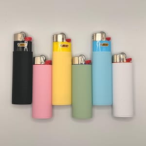 Può includere: Un set di sei accendini BIC nei colori nero, rosa, giallo, verde chiaro, azzurro e bianco. Ogni accendino presenta una parte superiore metallica con un pulsante di accensione rosso e un logo BIC rettangolare sulla parte superiore.