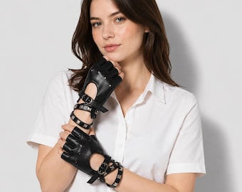 Op de afbeelding: Een paar zwarte vingerloze handschoenen van glad materiaal, voorzien van een uitsparing op de rug van de hand, verstelbare gespriemen bij de pols en een bijpassende armband met studs onder de manchet van de handschoen.