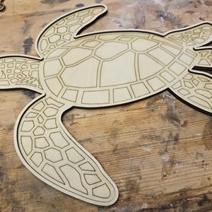 May include: A wooden sea turtle cut-out with a detailed shell pattern and black outline. The turtle's flippers and head are also cut out, creating a three-dimensional effect. The natural wood color contrasts with the dark outline.