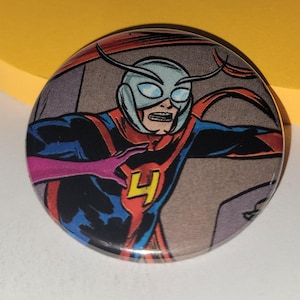 May include: A round button featuring a comic book illustration of a superhero in a mask and costume. The superhero is in a dynamic pose, with a red, blue, and yellow color scheme. The number "4" is prominently displayed on the chest.