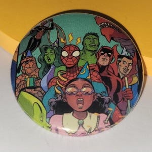 May include: Round button featuring a comic book illustration of various Marvel characters, including Spider-Man, Hulk, and Daredevil, with a central figure wearing glasses and a party hat. The button has a teal background.