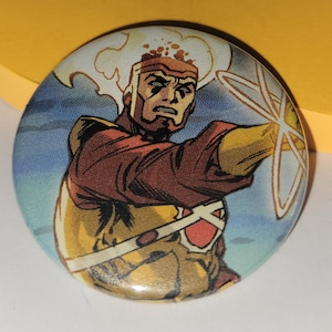May include: Round button featuring a comic book illustration of a superhero. The character has a stern expression, with a fiery white head and is wearing a brown and yellow costume. The background is blue with white clouds.