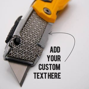 May include: A utility knife with a yellow and black handle and a silver blade. The knife has a geometric pattern on the side and the text "ADD YOUR CUSTOM TEXT HERE".