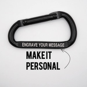 May include: Black carabiner with the text "ENGRAVE YOUR MESSAGE" and "MAKE IT PERSONAL". The carabiner is a metal clip used for attaching items, often used in outdoor activities. The carabiner is shown against a white background.